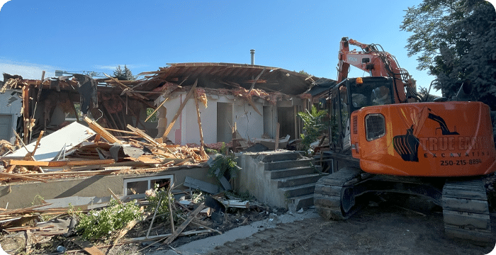 An excavator demolishes a house, highlighting the importance of hazardous material handling during construction